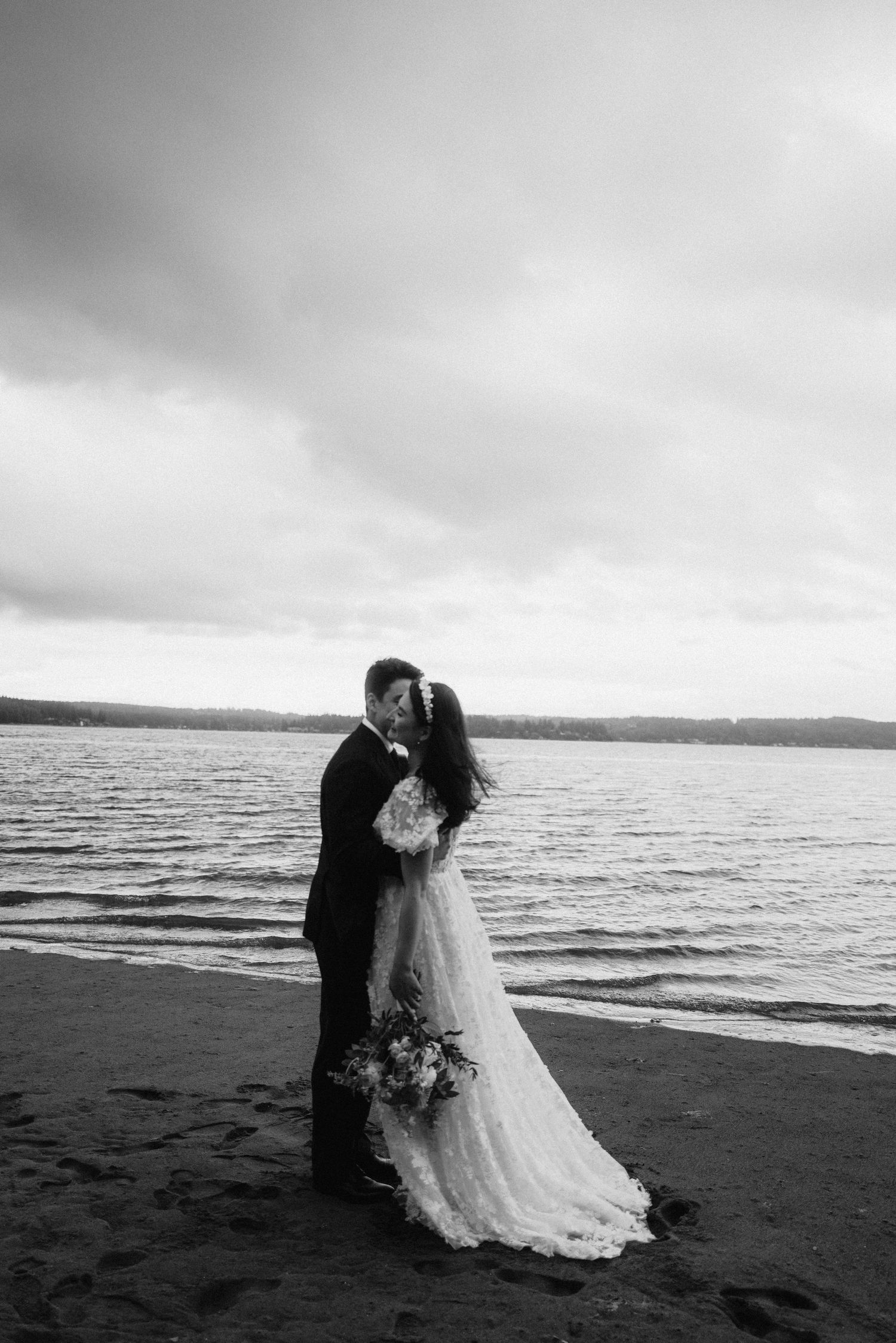 Black and white photo of couple sharing romantic moment on moody beach landscape.