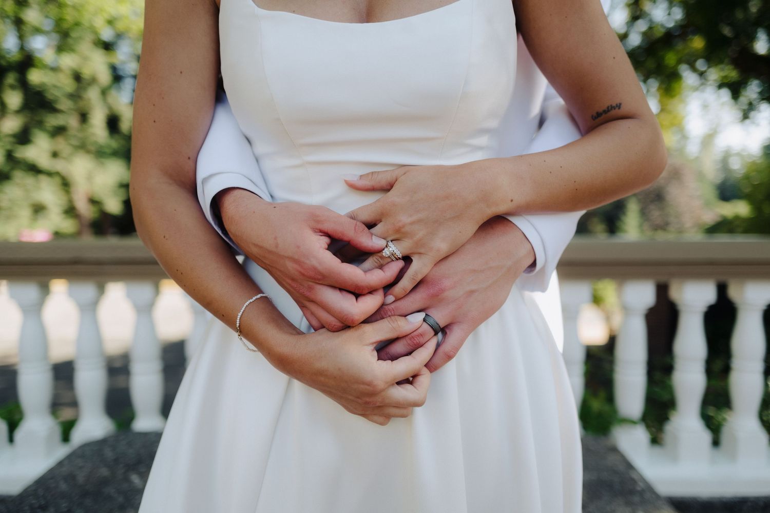 Close-up detail shot of hands clasped together while wearing a white wedding dress.