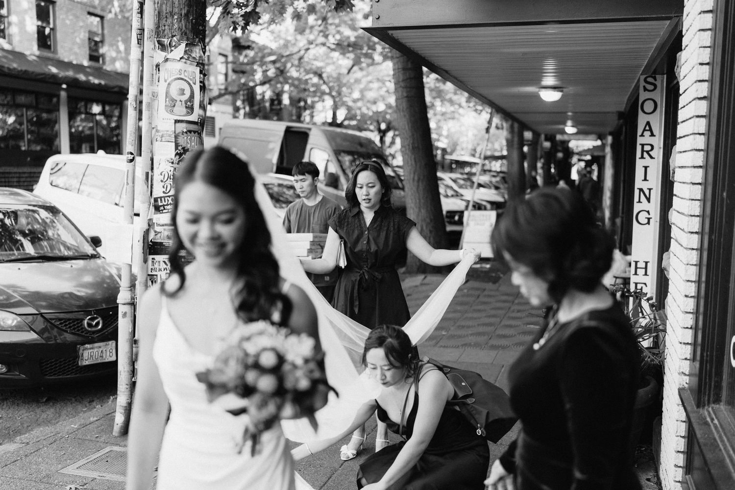 A bride with a bouquet walks under a covered sidewalk in a black and white candid moment.
