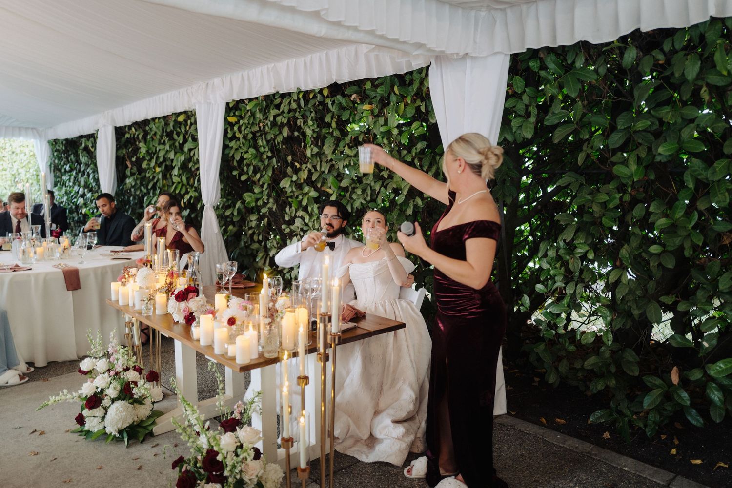 Wedding reception tent decorated with white draping and lush green foliage walls.