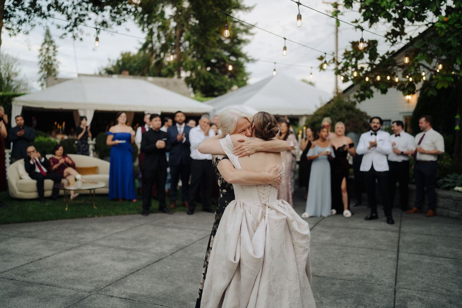 Wedding guests gather on an outdoor patio under string lights during a reception.