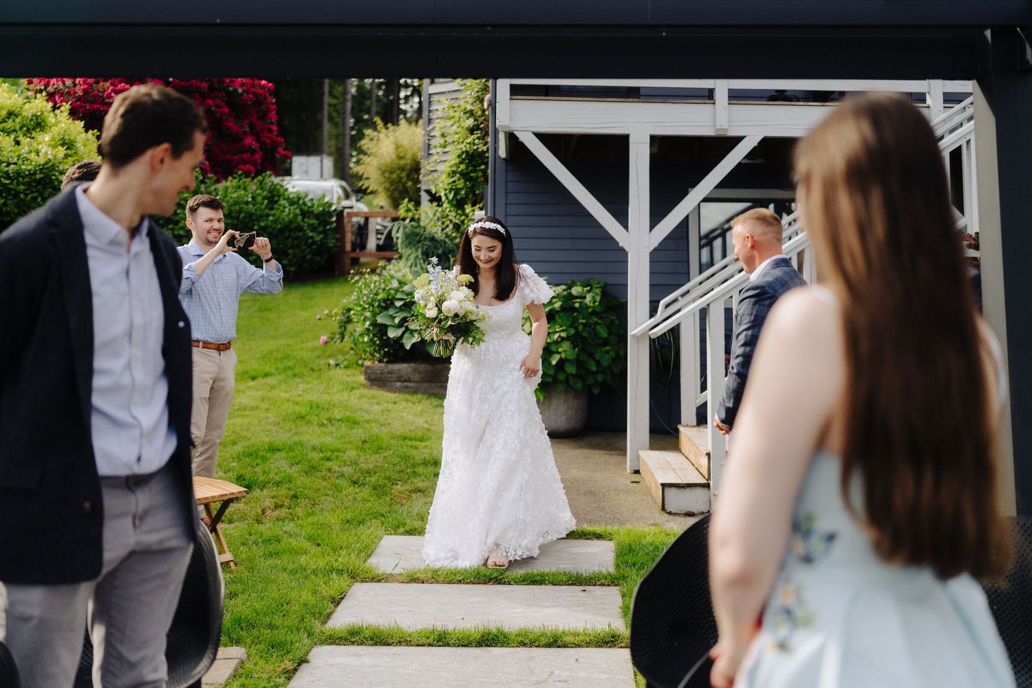 Outdoor wedding ceremony setup with white chairs and floral arrangements under a wooden pergola by the water.