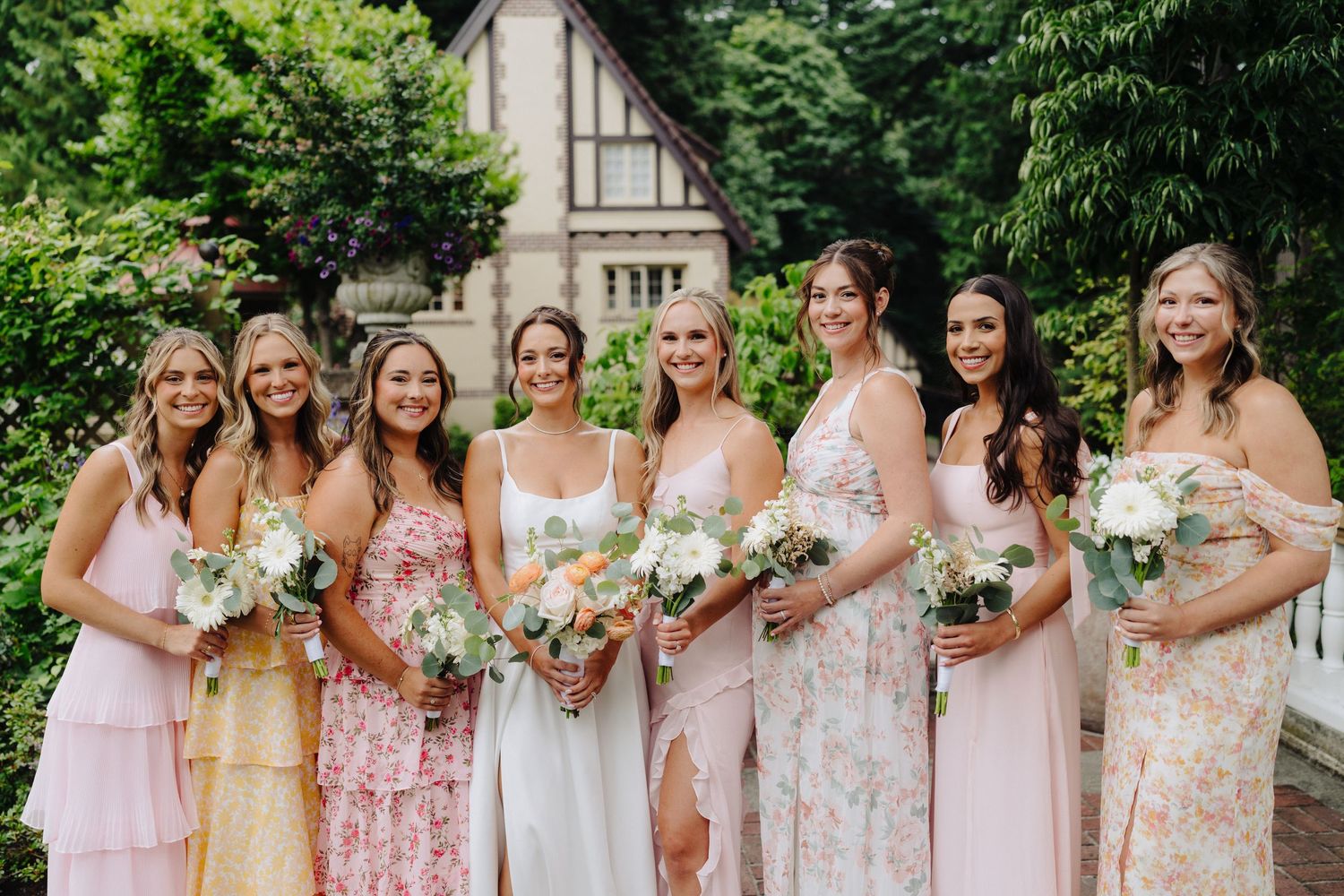 Wedding party in pink and floral dresses posing together in a garden setting.