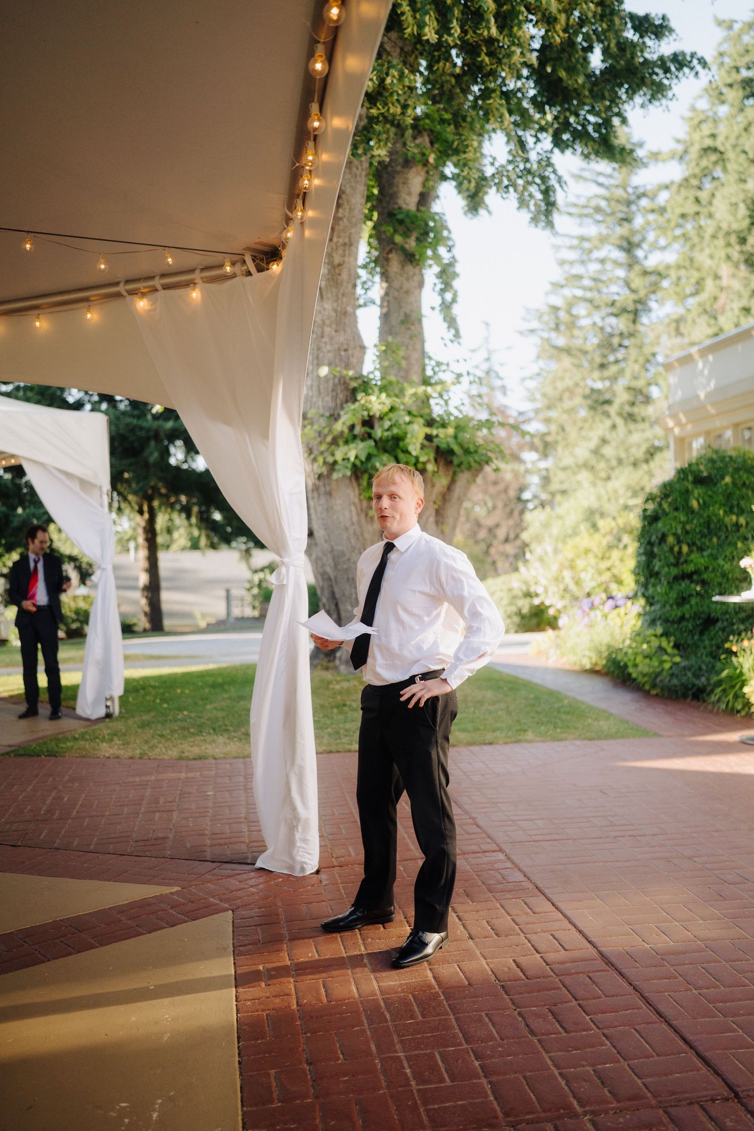 Person in formal attire standing under string lights at outdoor wedding reception.