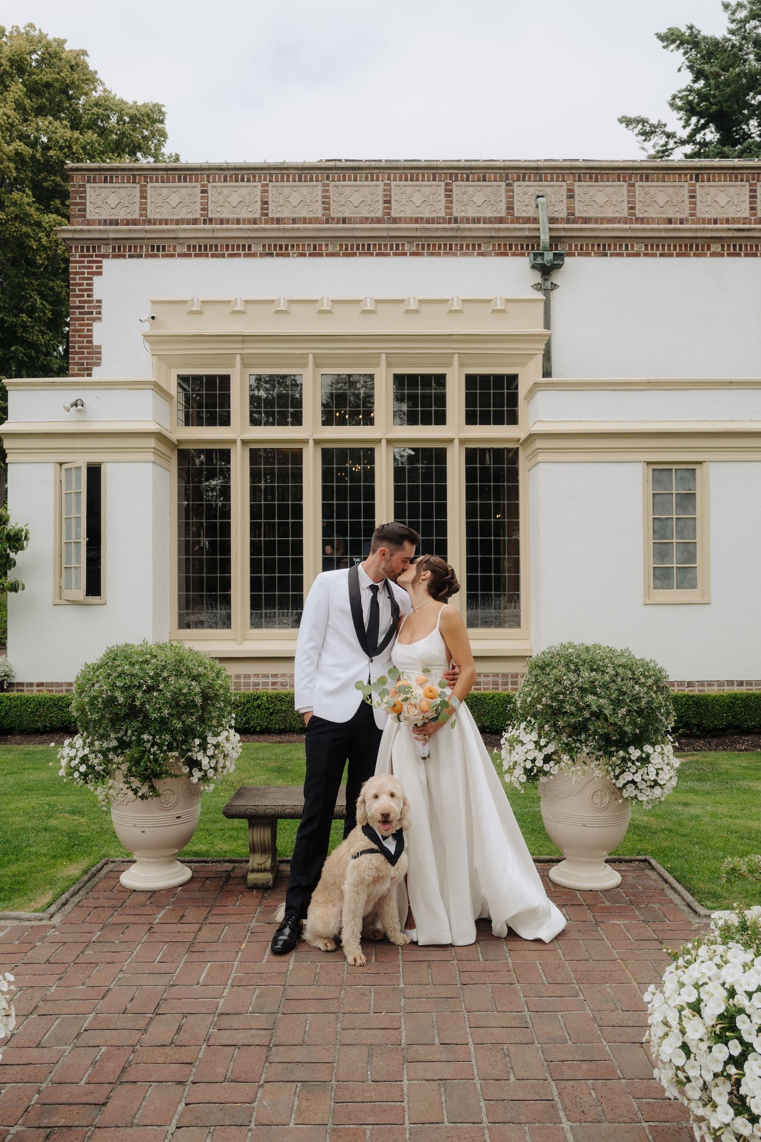 Elegant wedding photo featuring a couple and their golden retriever in front of a classical white building.