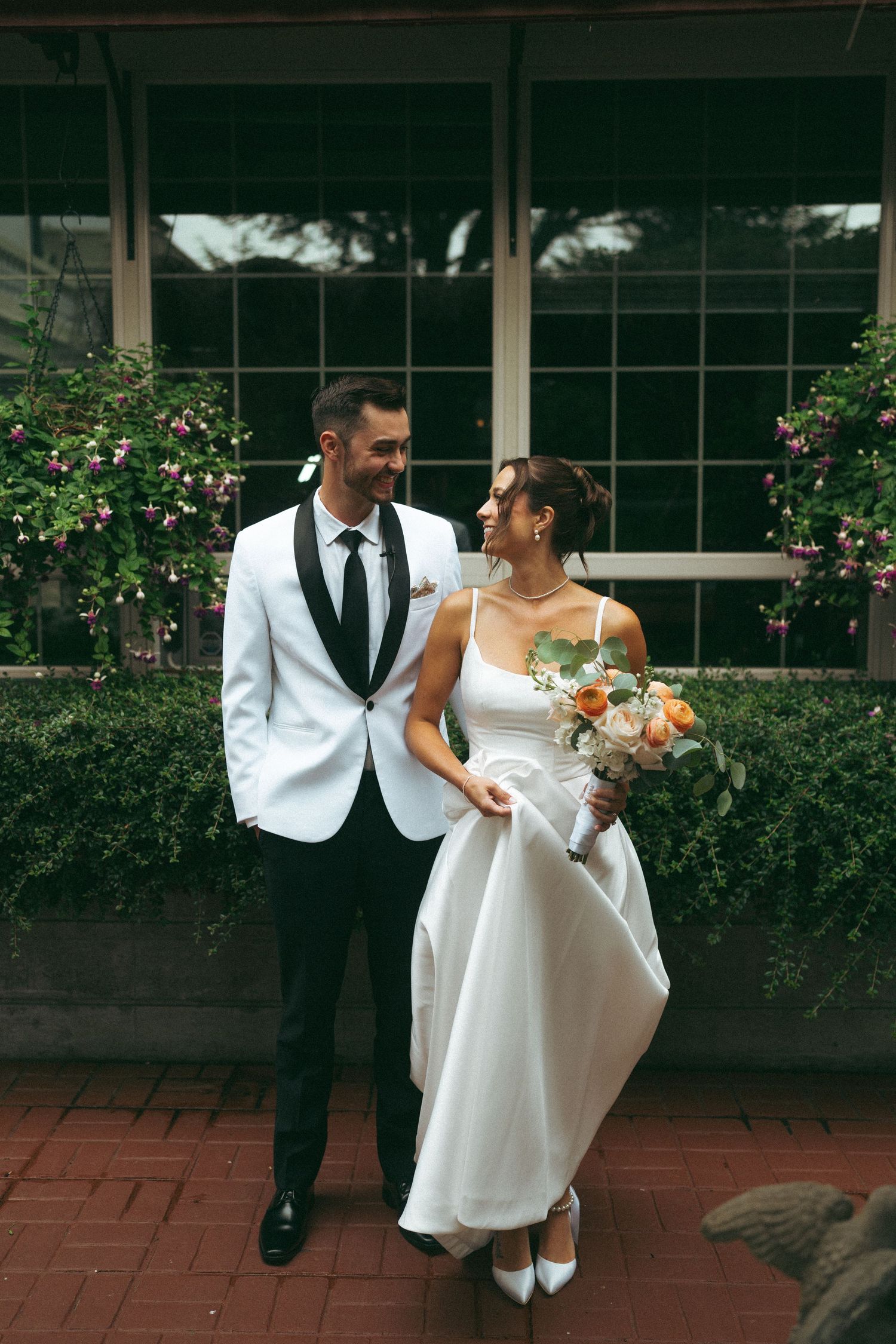 Candid wedding moment captured in front of window with pink flowering bushes and brick path.