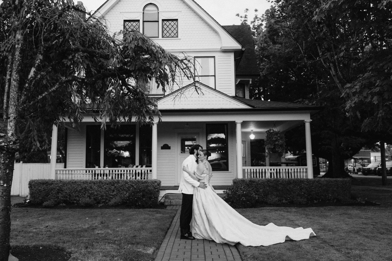 Panoramic black and white view of historic white house with wraparound porch.