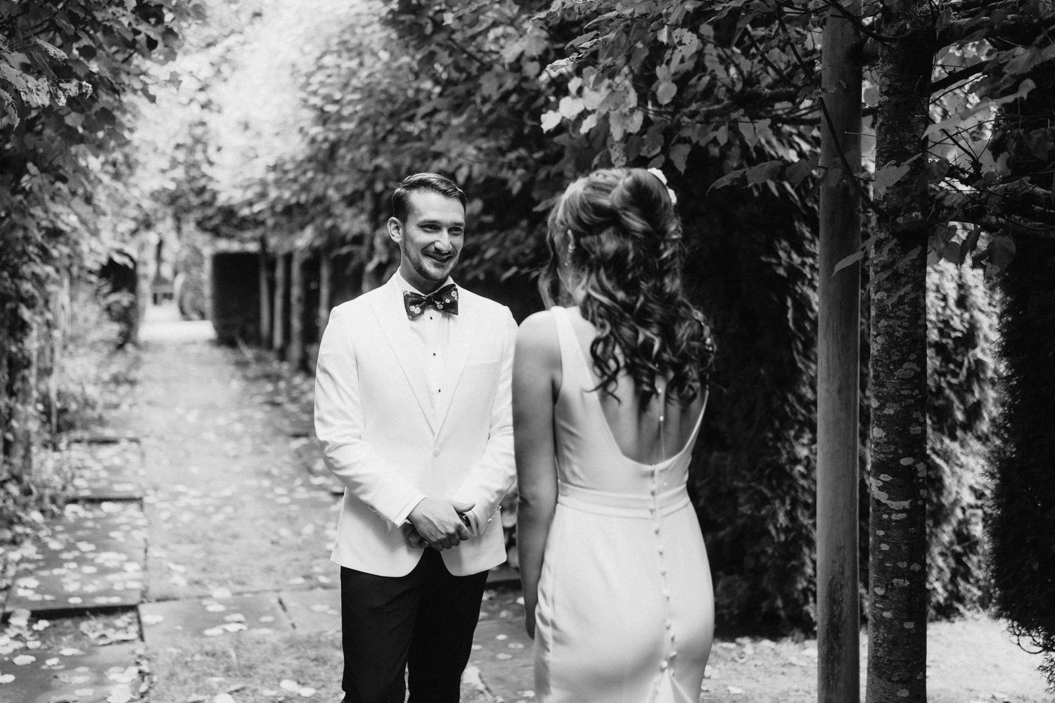 Black and white photo of couple in formal attire walking along a tree-lined path.