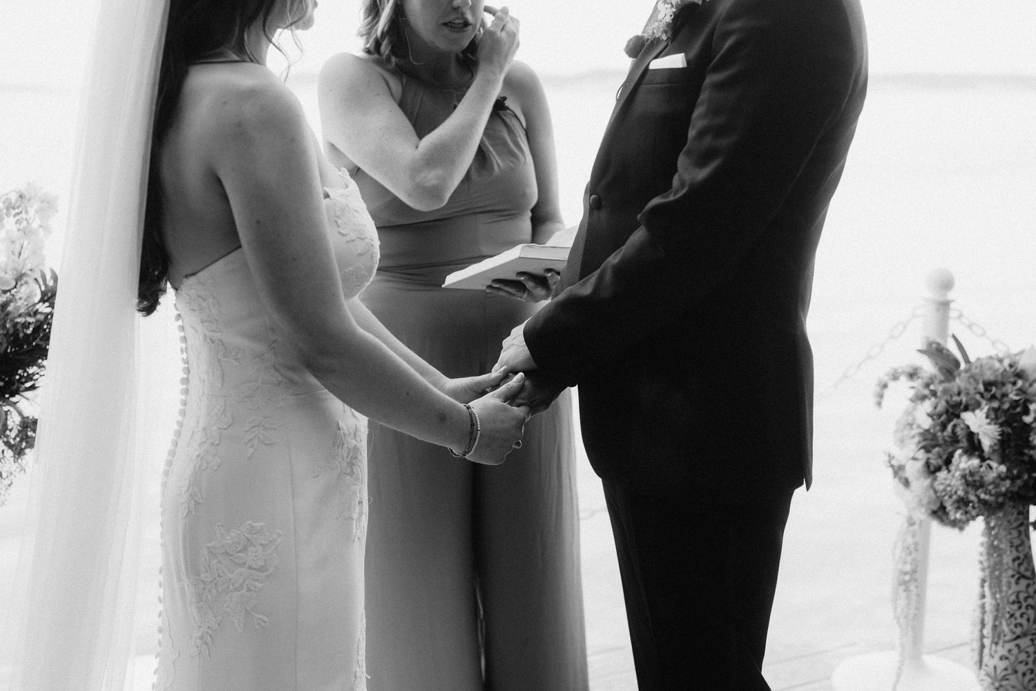 Black and white wedding ceremony photo showing couple exchanging vows outdoors.