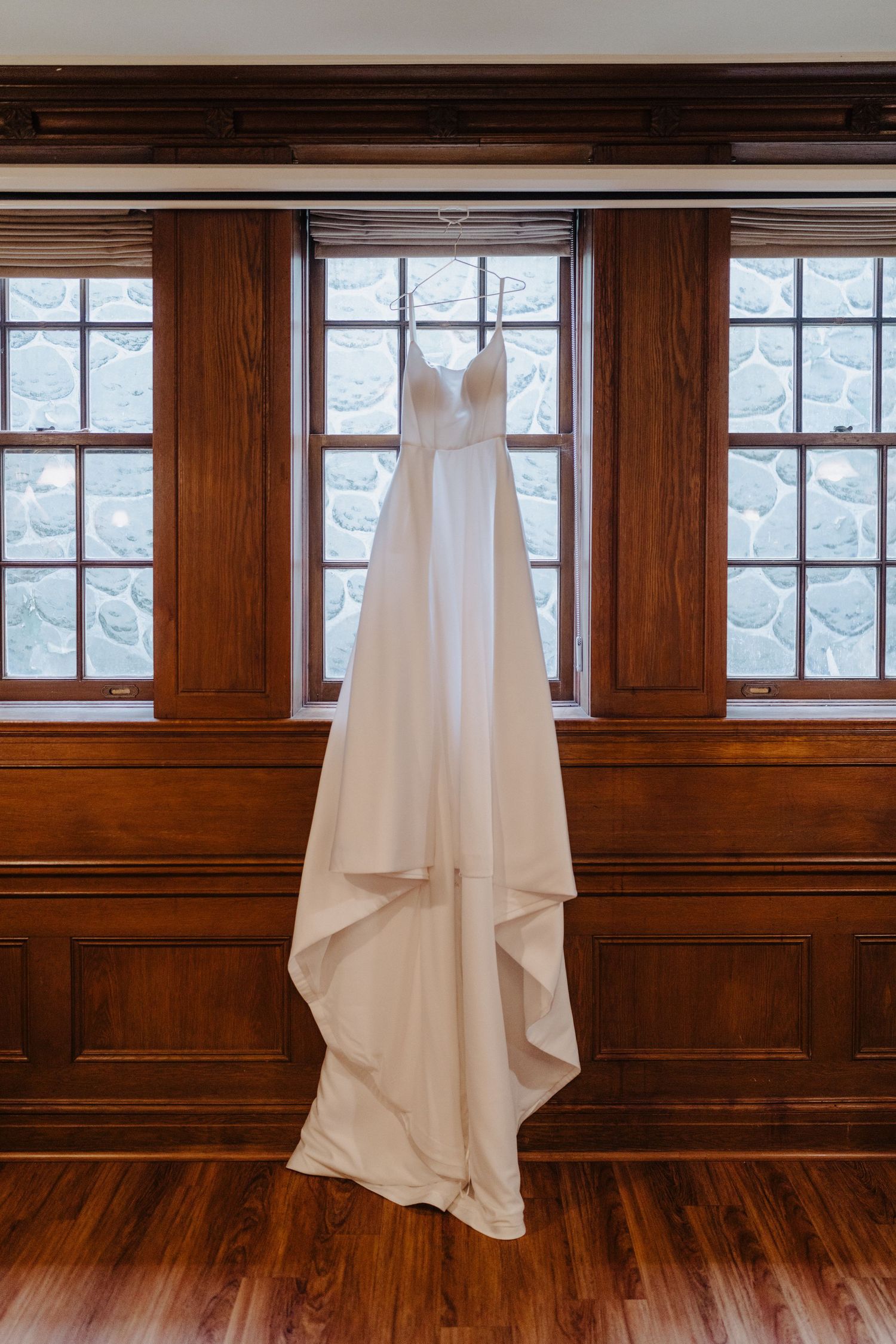 White wedding dress displayed hanging against wooden paneled walls in elegant venue.