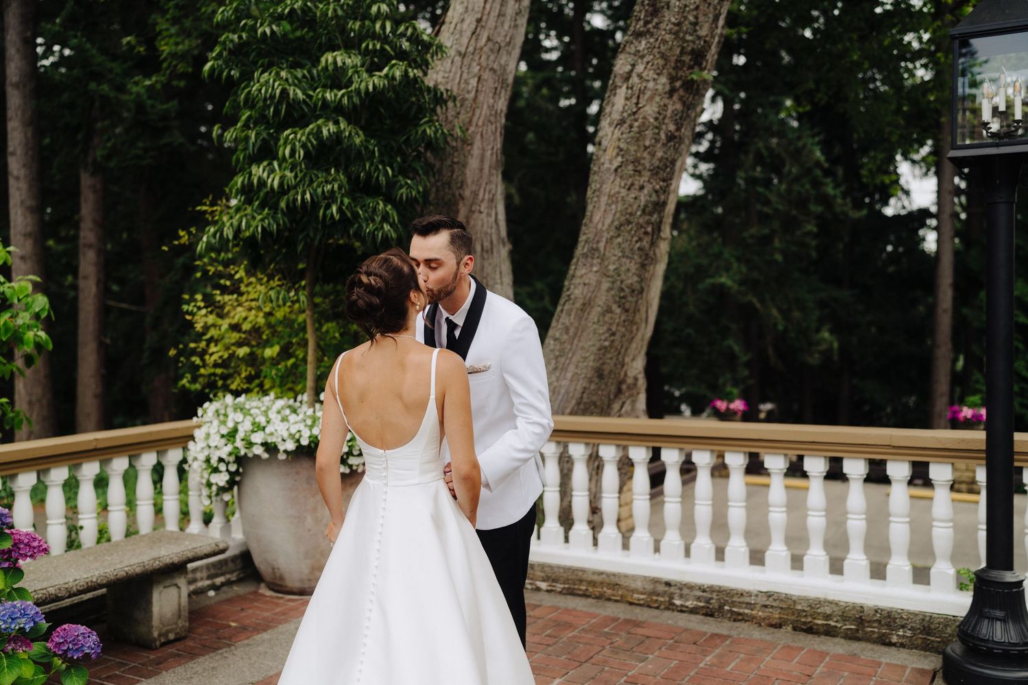 A bride and groom share intimate moments in a garden setting with white picket fences and lush trees.