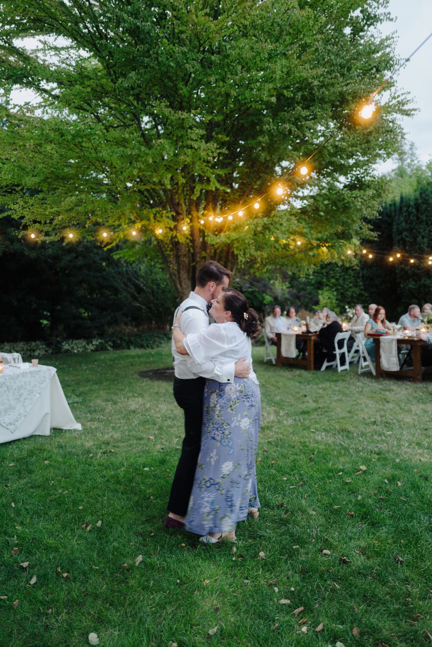 Couples dancing at twilight under string lights during an outdoor garden wedding reception.