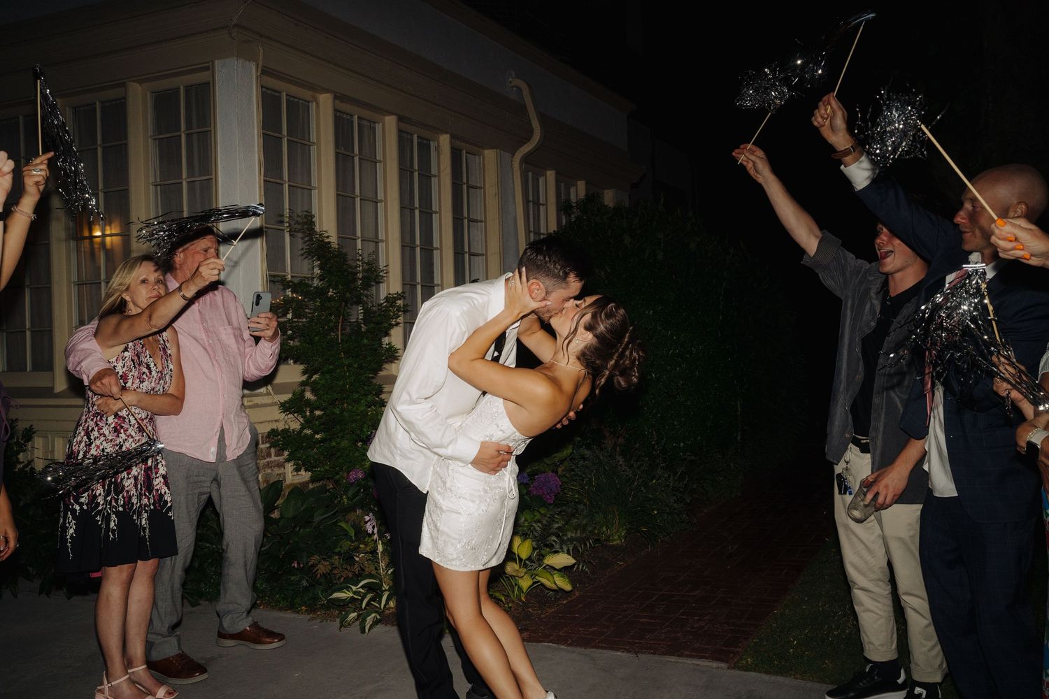 Night wedding exit with guests holding sparklers as couple shares romantic moment.