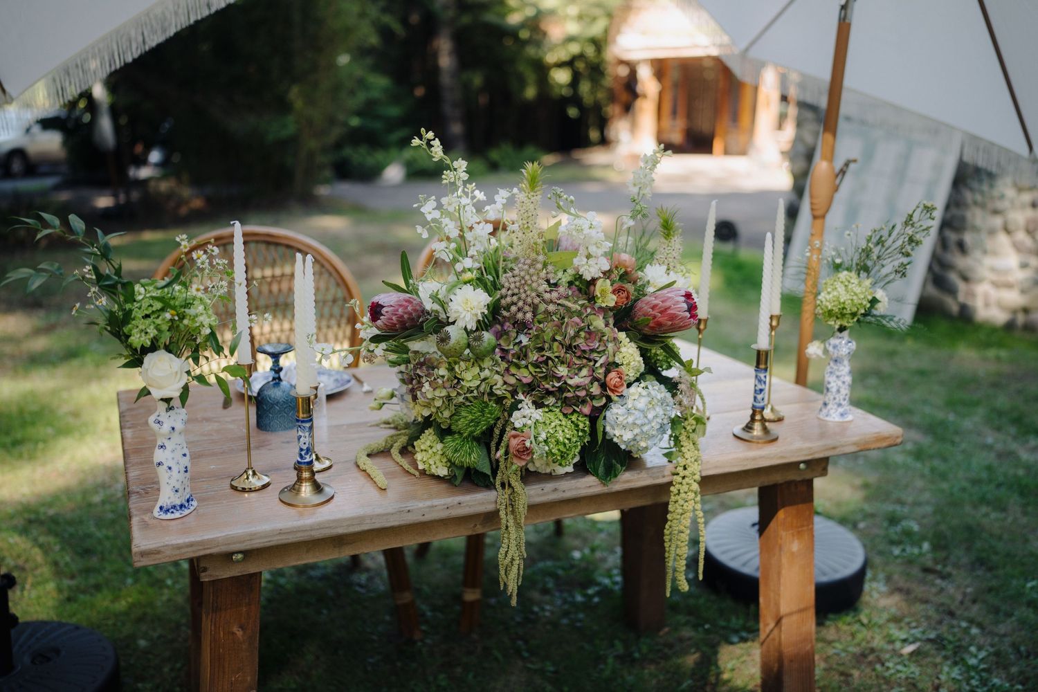 An outdoor wedding reception setup with wooden tables decorated with floral arrangements and candles.