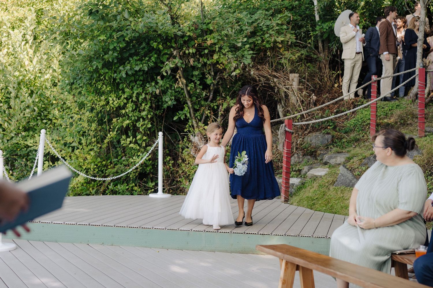 Wedding ceremony taking place on a scenic waterfront deck surrounded by greenery.