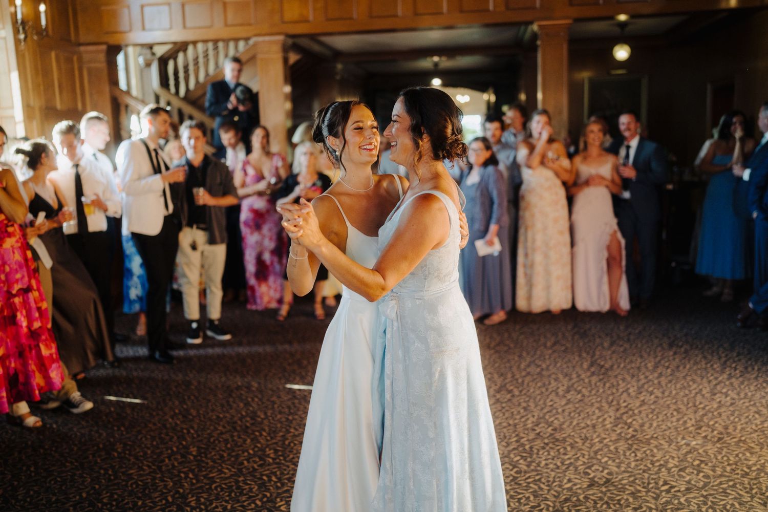 Wedding celebration features dancing in an elegant wood-paneled reception hall with chandeliers.