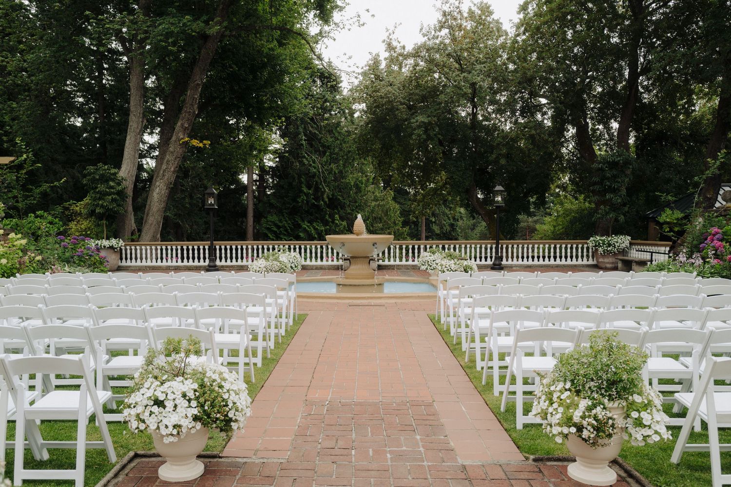 An outdoor wedding ceremony setup with white chairs and floral arrangements along a brick pathway.
