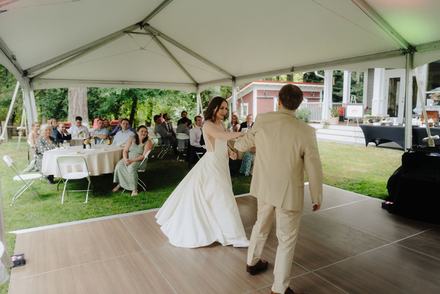 Outdoor wedding reception under white tent canopy with guests mingling.
