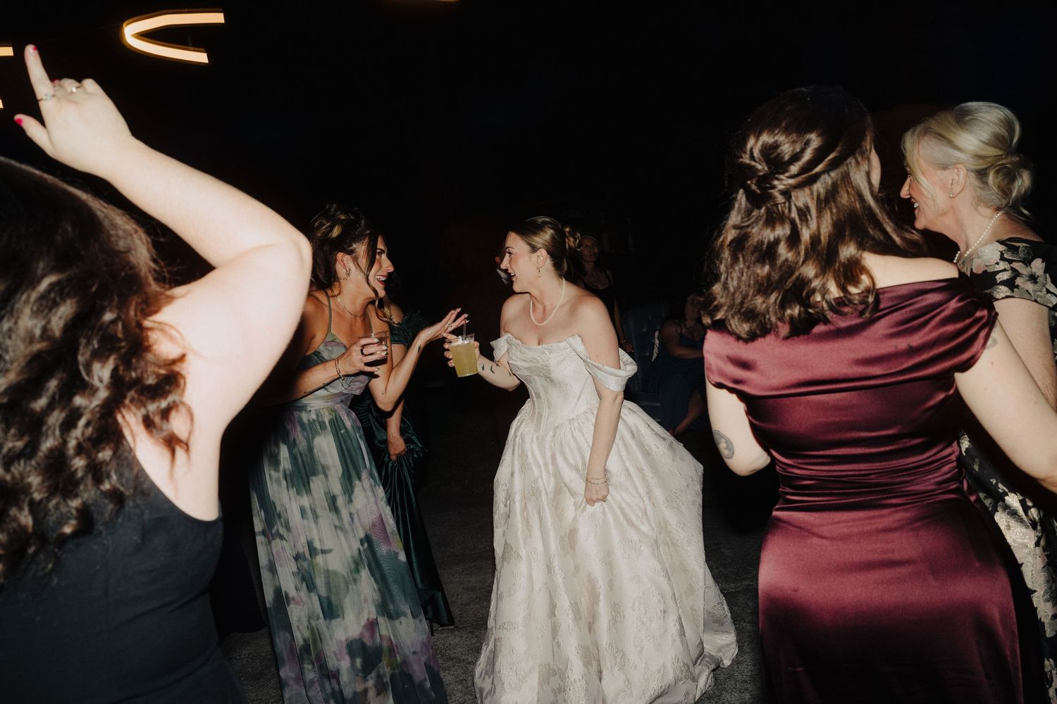 Wedding reception guests dance and celebrate on a dimly lit dance floor.