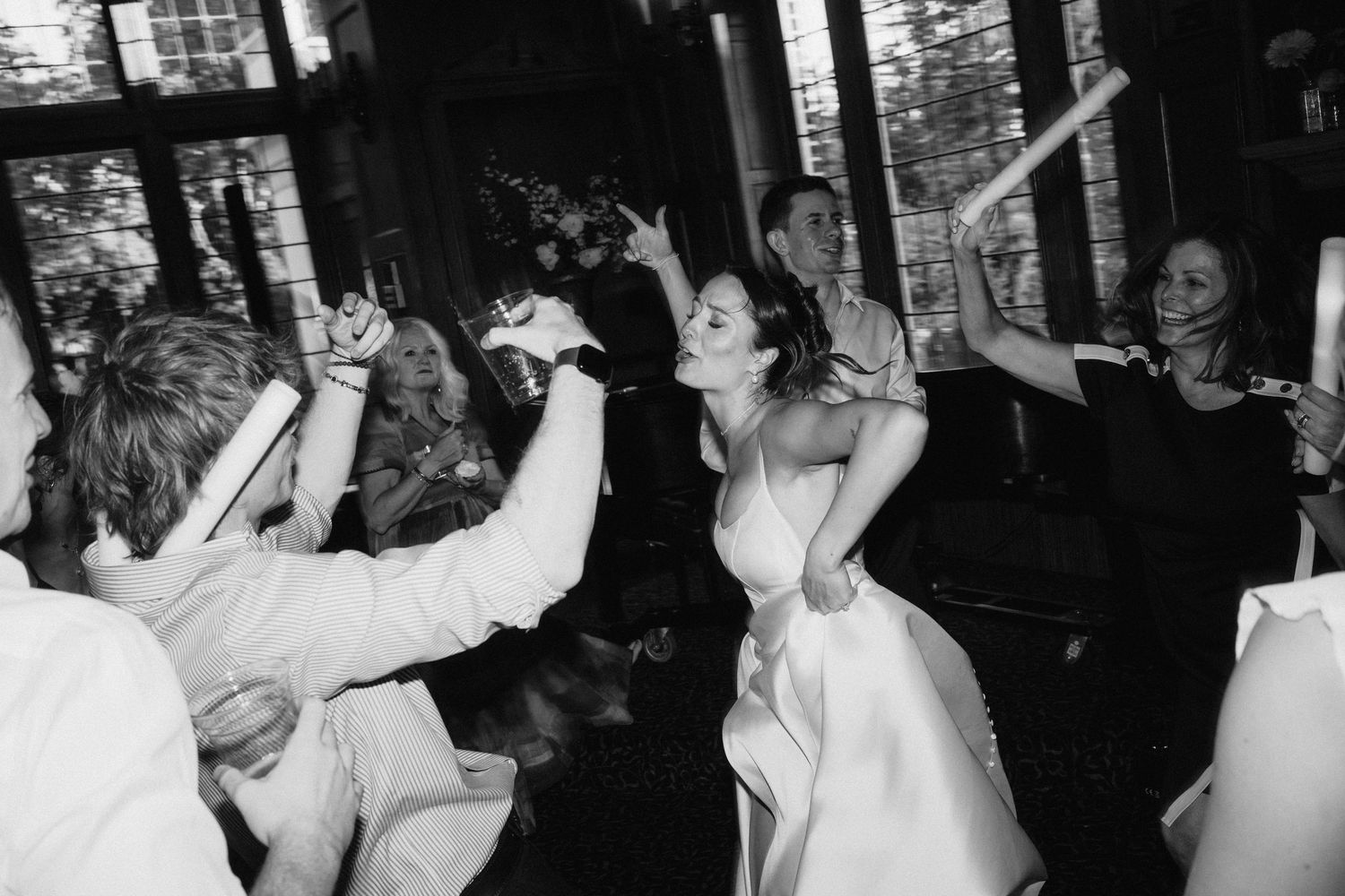 Wedding reception guests dancing and celebrating on a dark dance floor with arms raised.