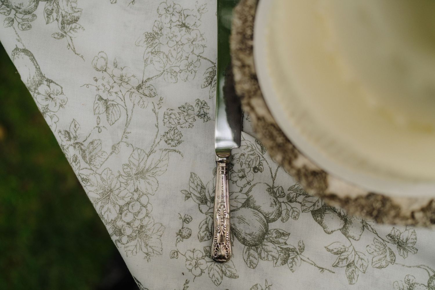 Close-up details of a wedding cake on a delicate floral patterned tablecloth.