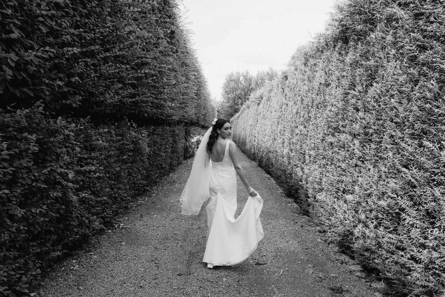 Black and white wedding photos taken along a hedge-lined garden path.