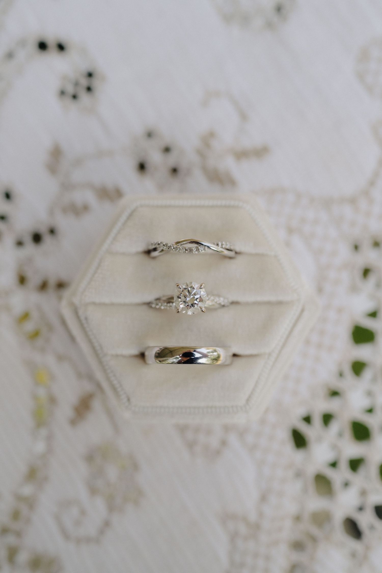 Close-up shots of delicate diamond engagement rings displayed on cream-colored cushions.