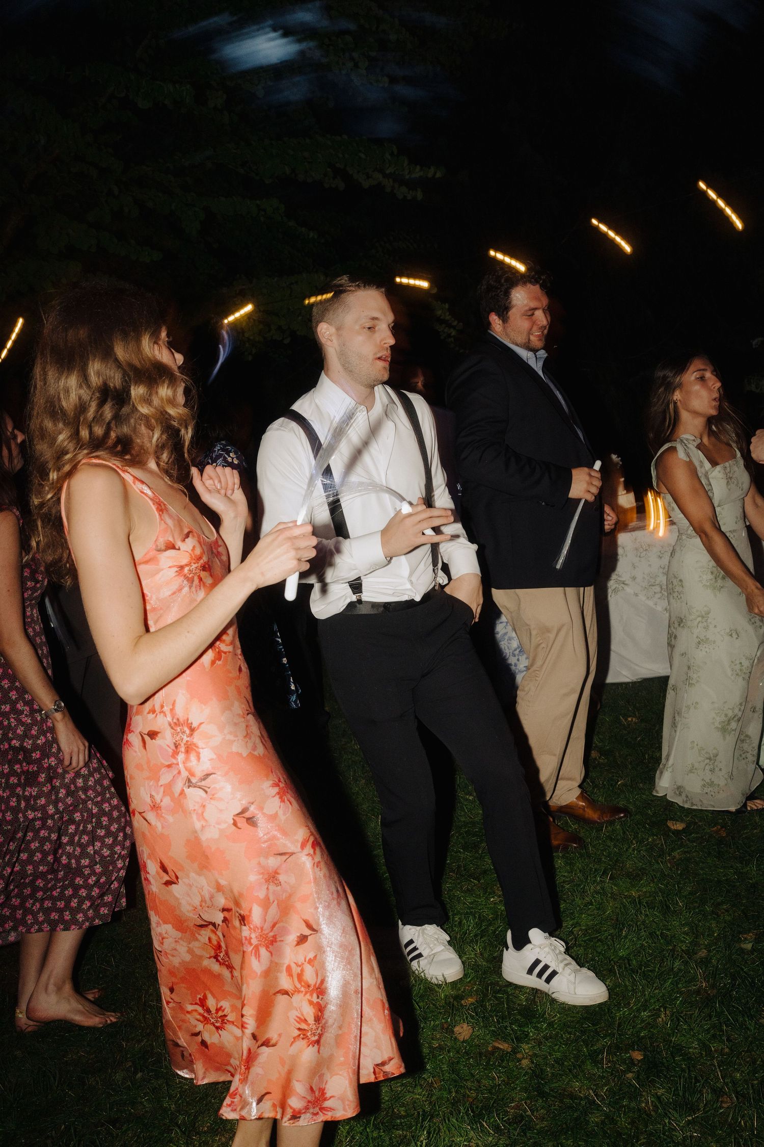 Wedding guests dance and celebrate at an outdoor evening reception with string lights overhead.