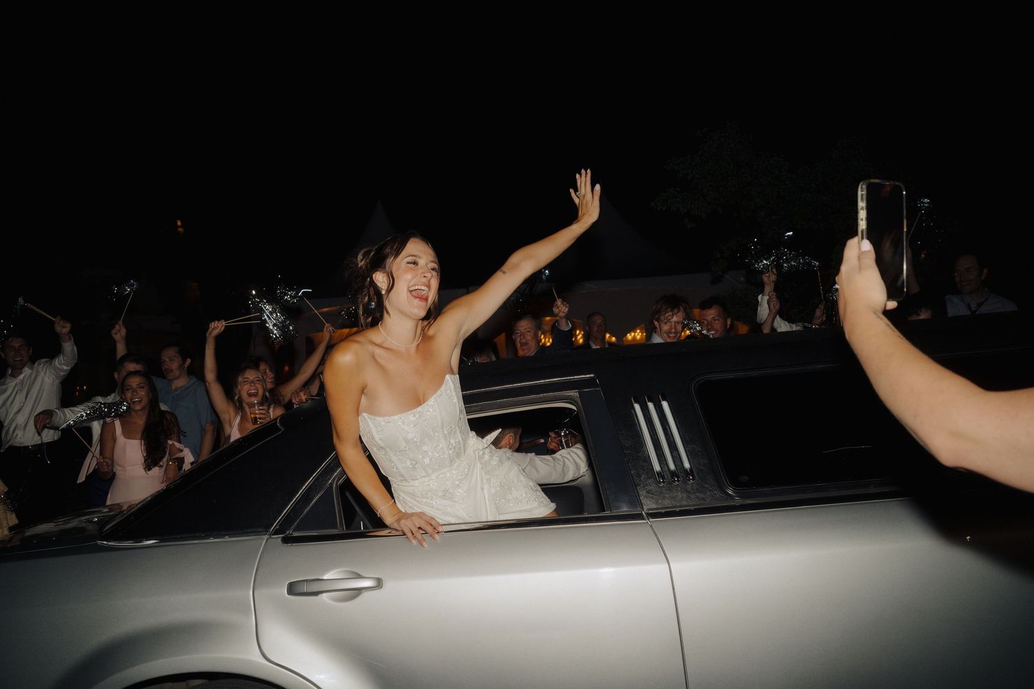 Wedding party exits in classic car during nighttime departure.