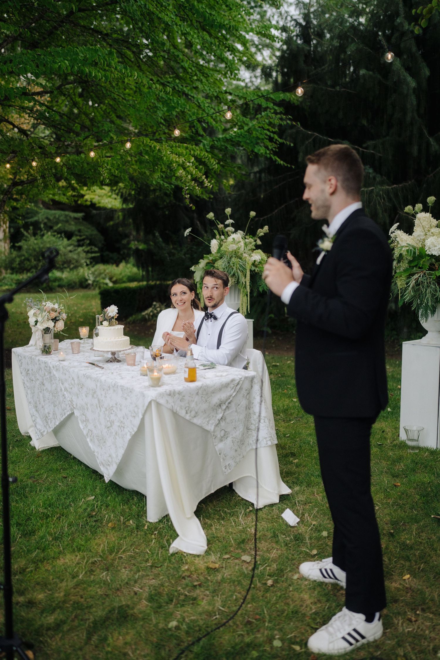 Wedding speech being given at outdoor reception with head table and string lights.