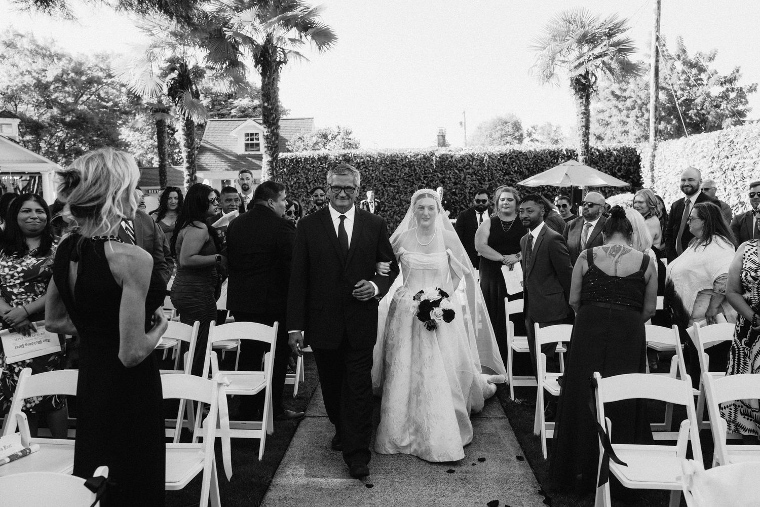 Black and white wedding ceremony photos arranged in a filmstrip style showing outdoor venue moments and processions.
