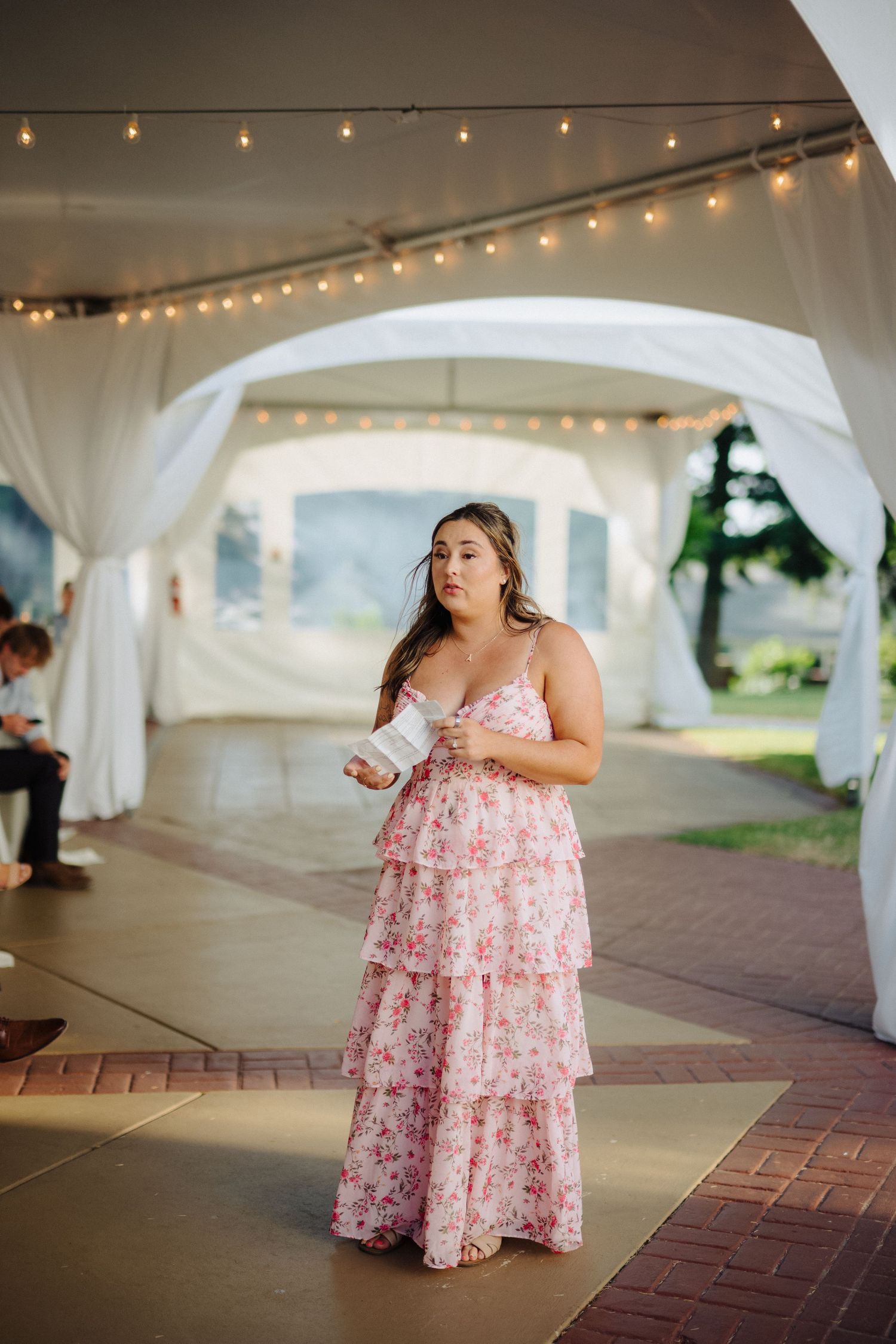Wedding guest in pink floral dress dancing under string lights in white tent reception.