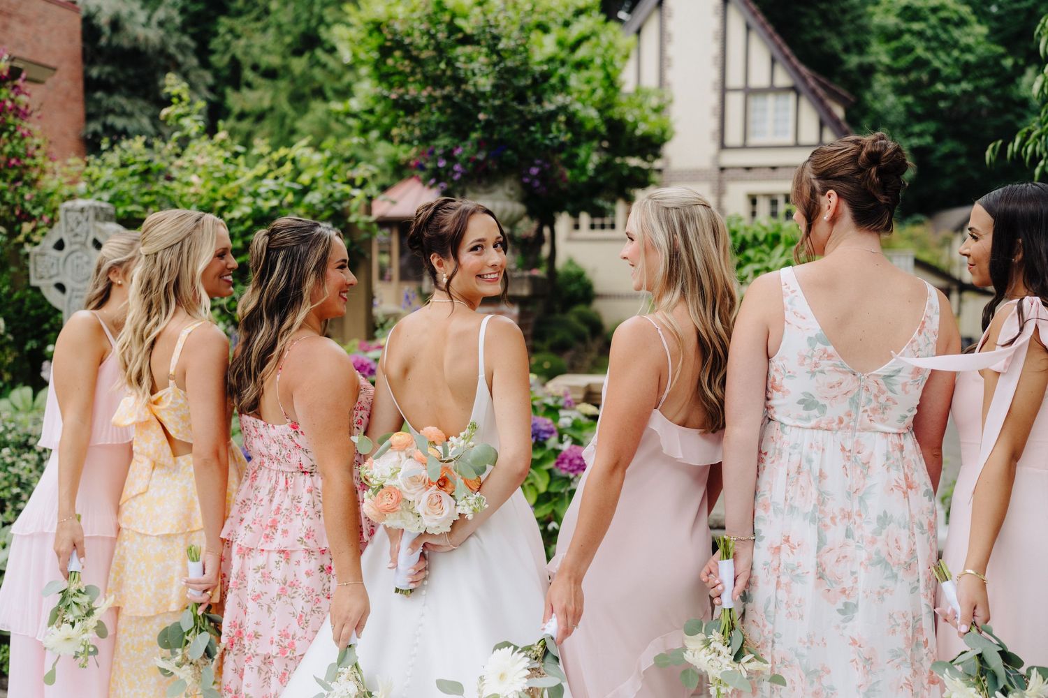 Bridesmaids in pink floral dresses walking together in a garden setting during a wedding celebration.