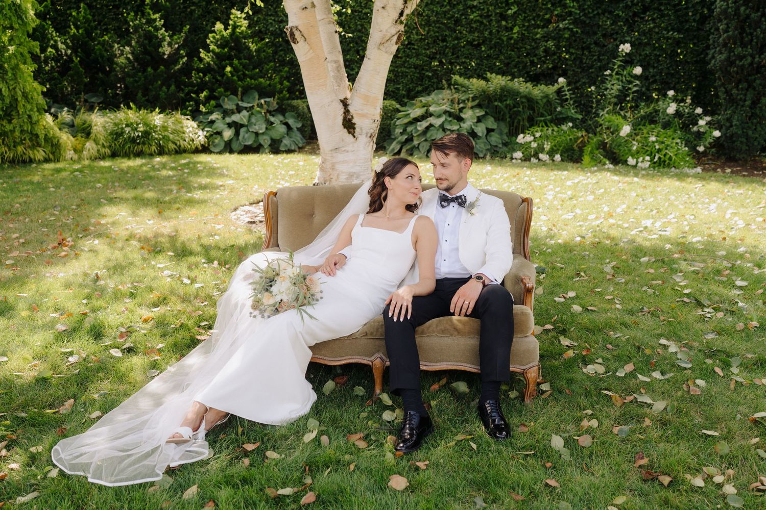 A couple shares a romantic moment on an antique sofa placed on a sunny garden lawn.