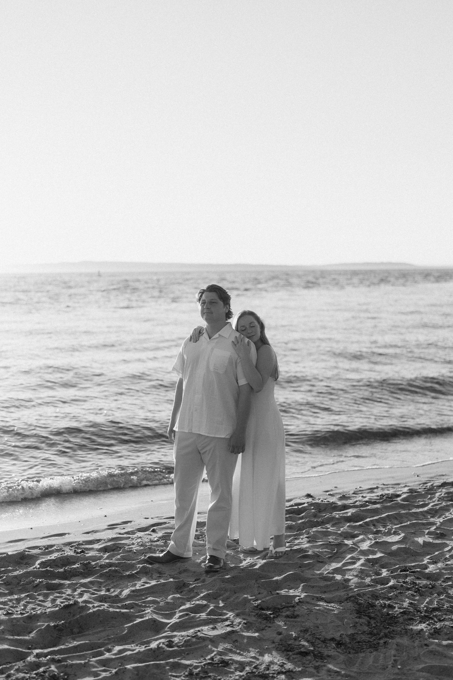 Couple in white outfits walking together along a misty beach shoreline.