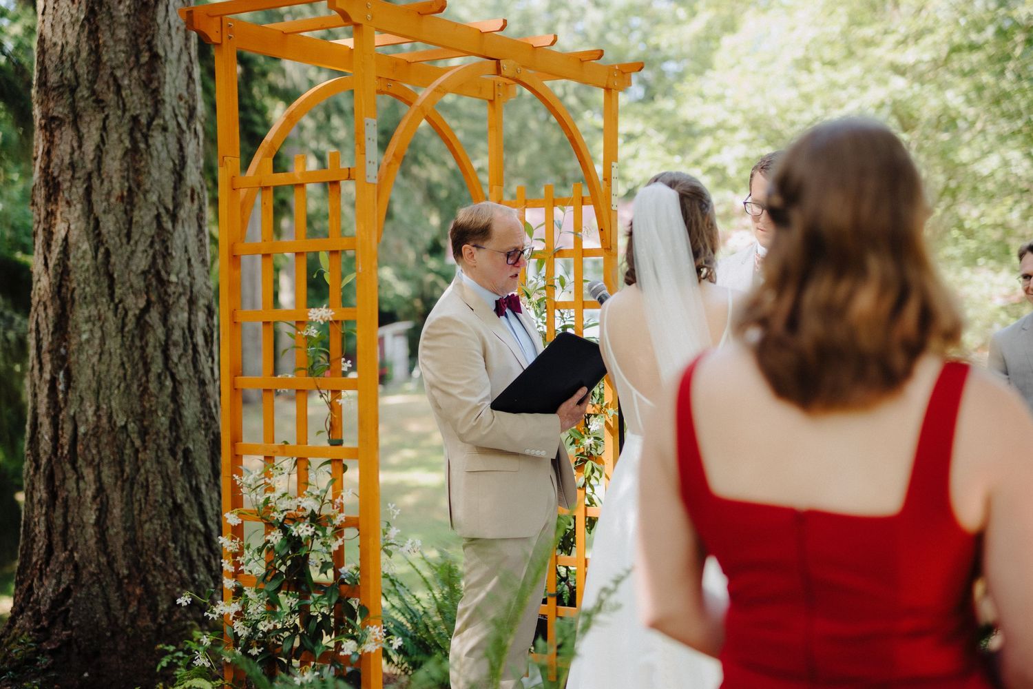 Wedding ceremony under an orange wooden arch decorated with flowers in a forest setting.