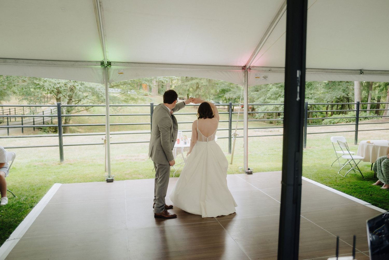 A couple sharing their first dance under a white tent at an outdoor wedding reception.