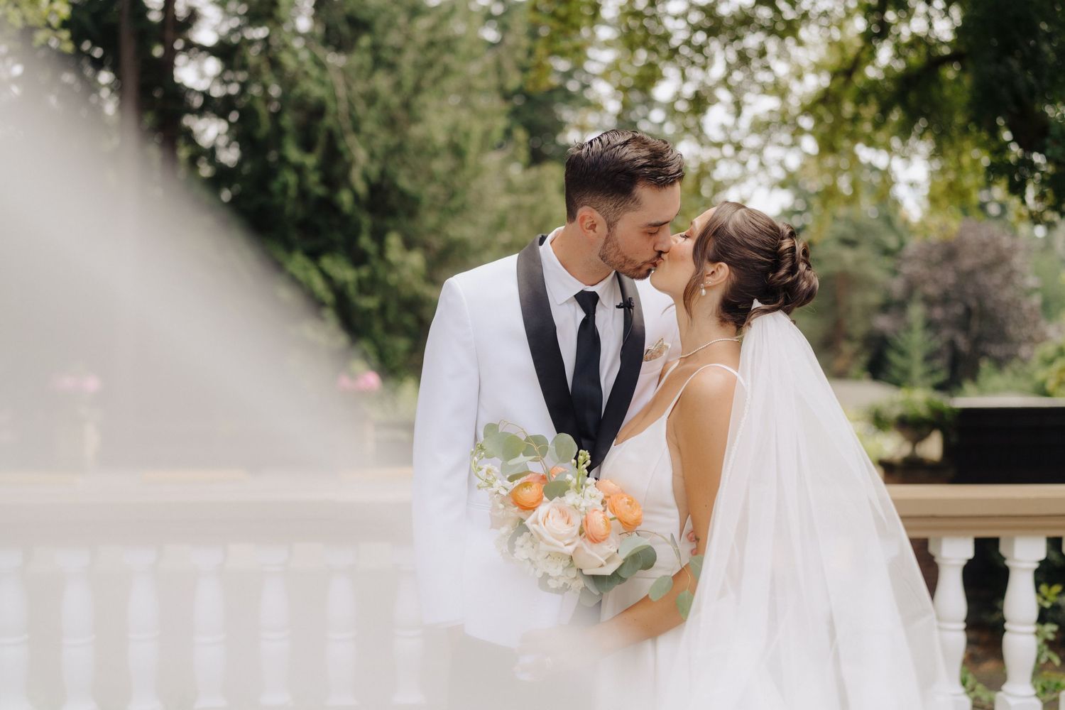 Couple shares intimate moment on terrace with peach bouquet and elegant attire.