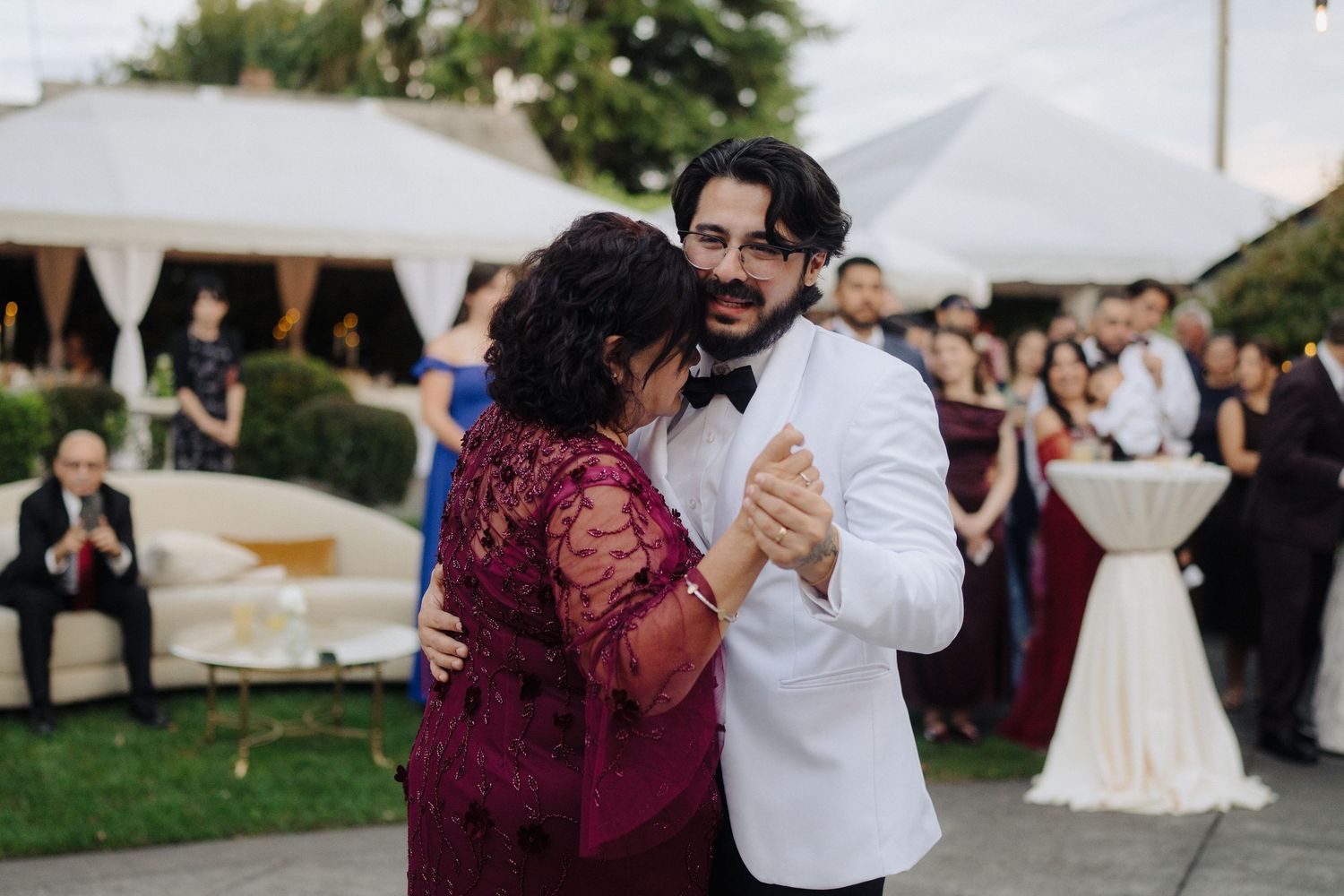 Wedding guests dancing in pairs under white tent during outdoor evening reception.