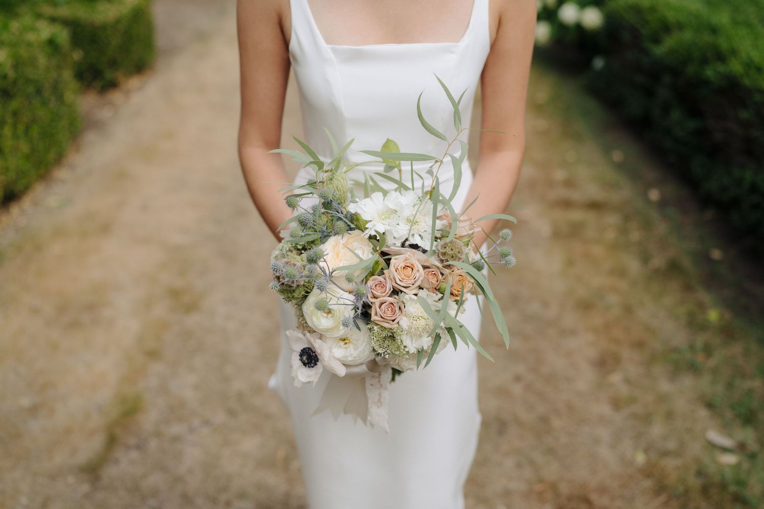 Close-up of a white wedding dress and delicate pastel floral bouquet.