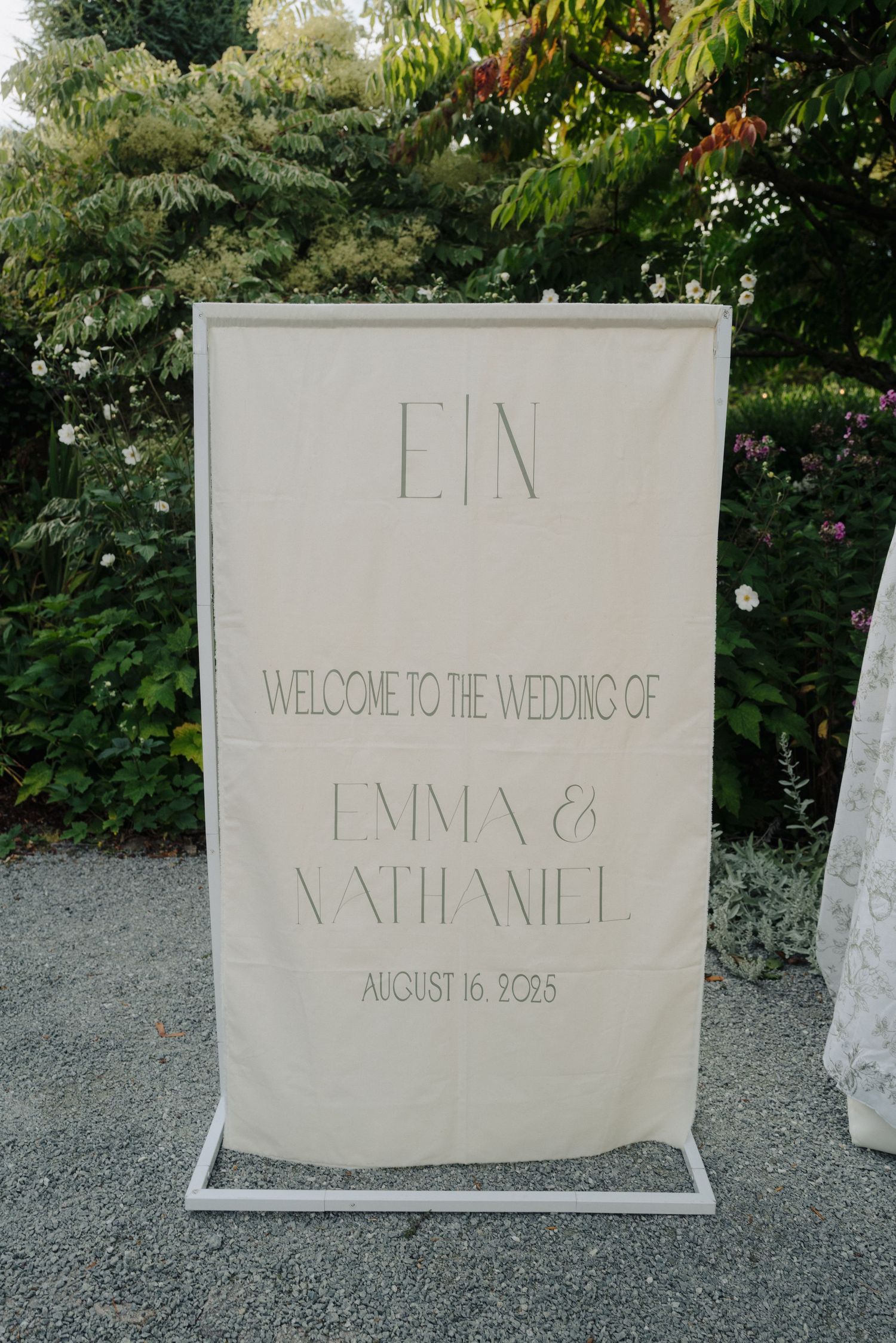 Elegant white wedding welcome sign with minimalist lettering displayed in an outdoor garden setting.