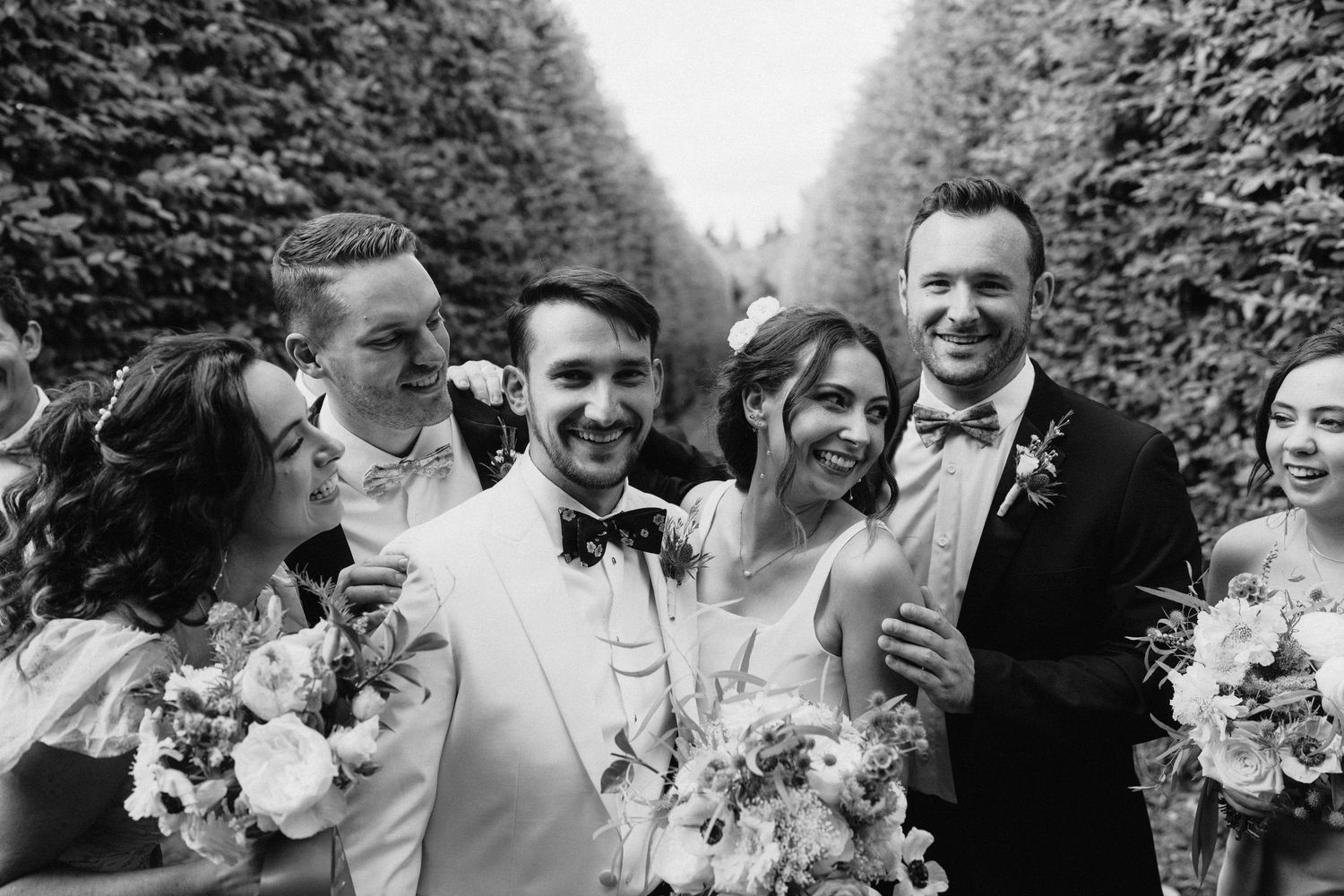 Black and white photo of wedding party laughing together outdoors.