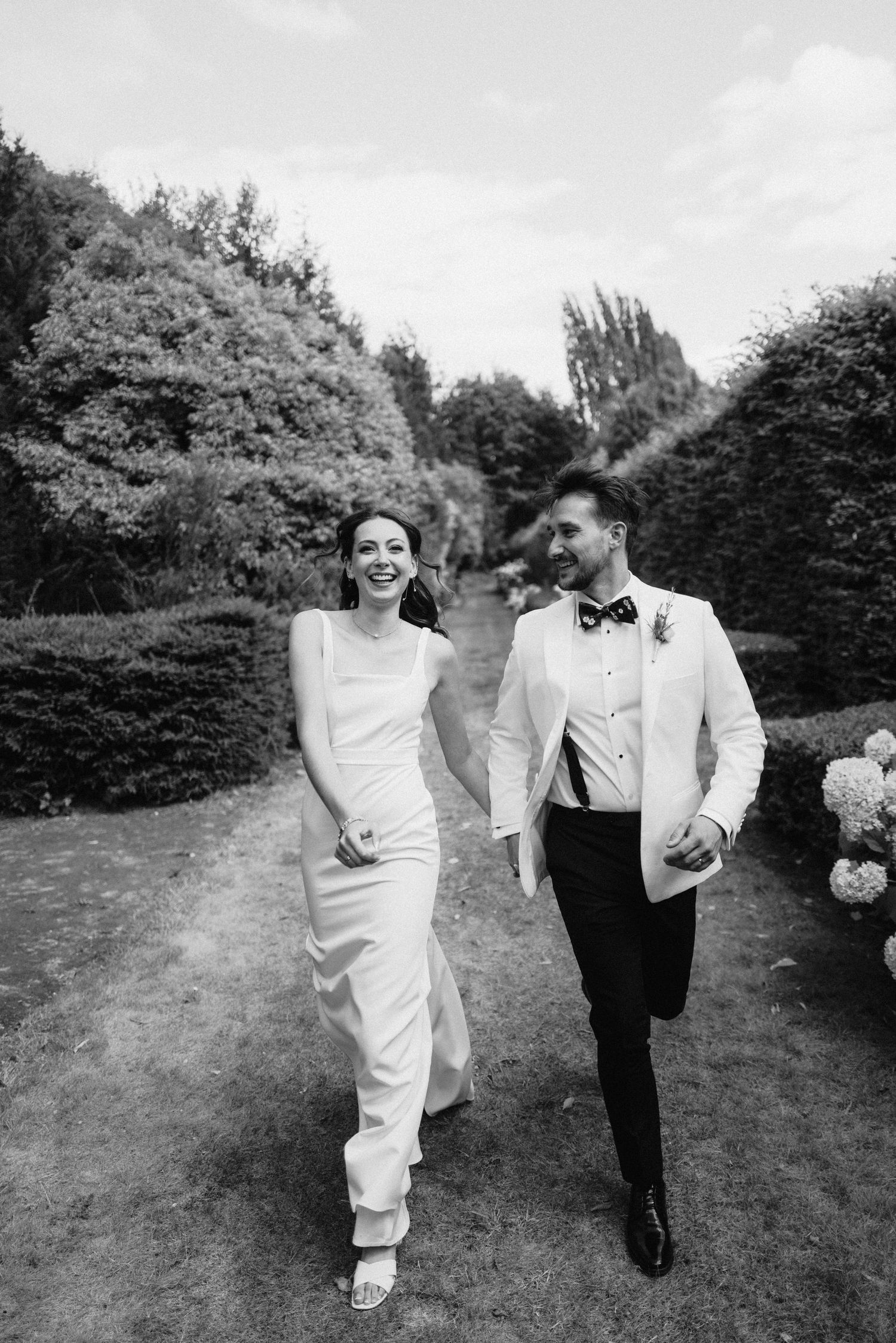 Couple walking and laughing together on a garden path during their wedding celebration.