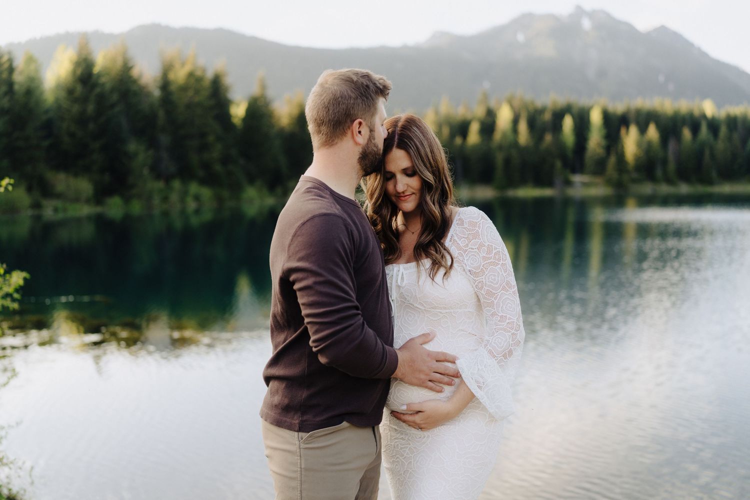 A tender maternity moment shared beside a peaceful mountain lake at sunset.