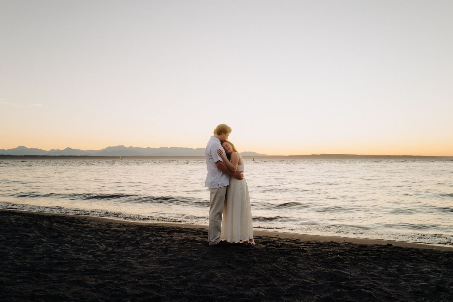 Silhouette of couple embracing on beach during golden sunset.
