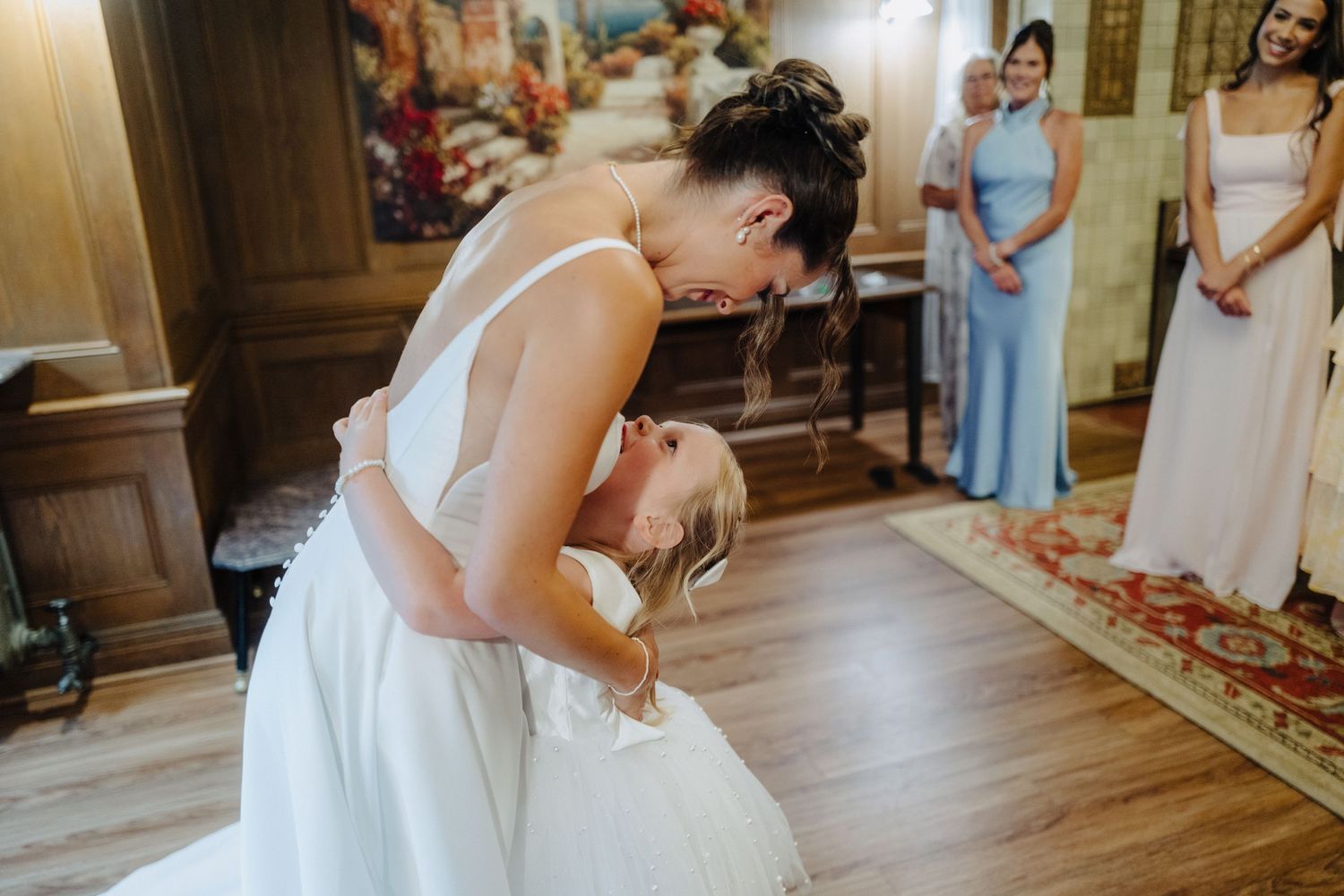 A bride and groom share their first kiss during a wedding ceremony in an elegant wood-paneled room.