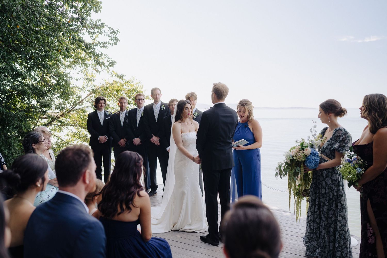 Outdoor wedding ceremony taking place on a scenic deck overlooking a waterfront view.