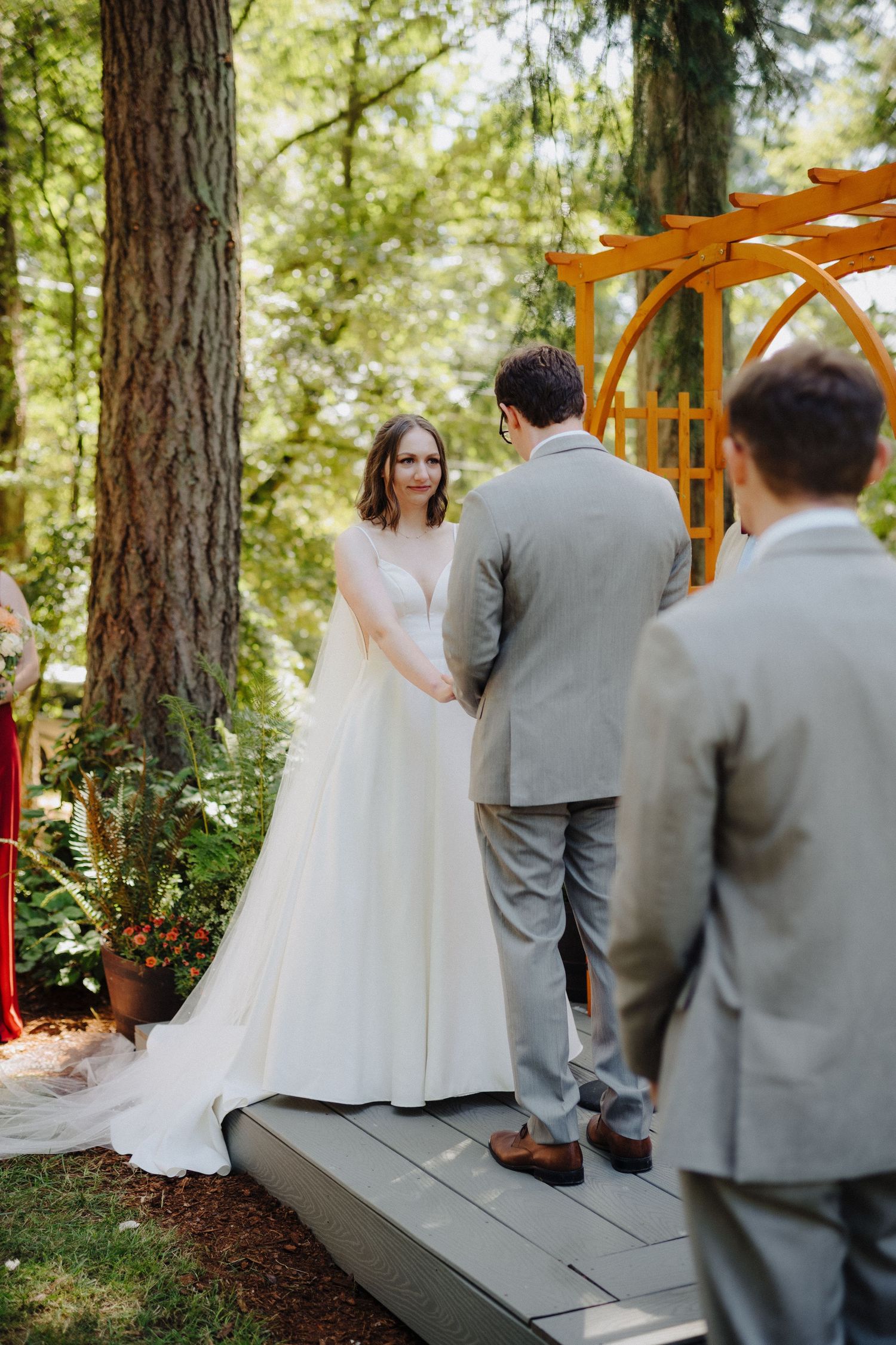 Wedding ceremony taking place under tall pine trees with a wooden arch and floral decorations.