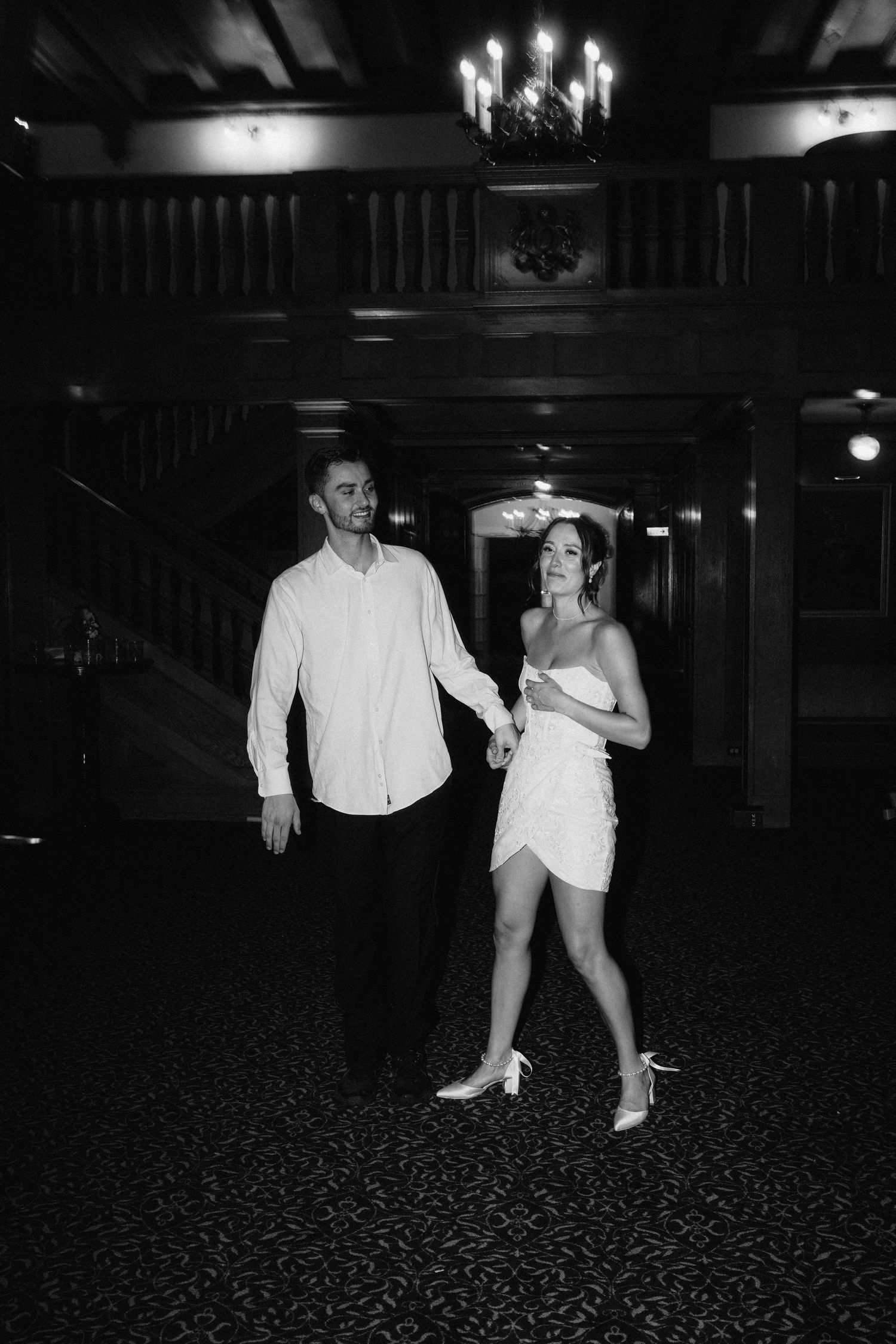 Black and white photo of a couple dancing in a dimly lit ballroom with a patterned carpet.