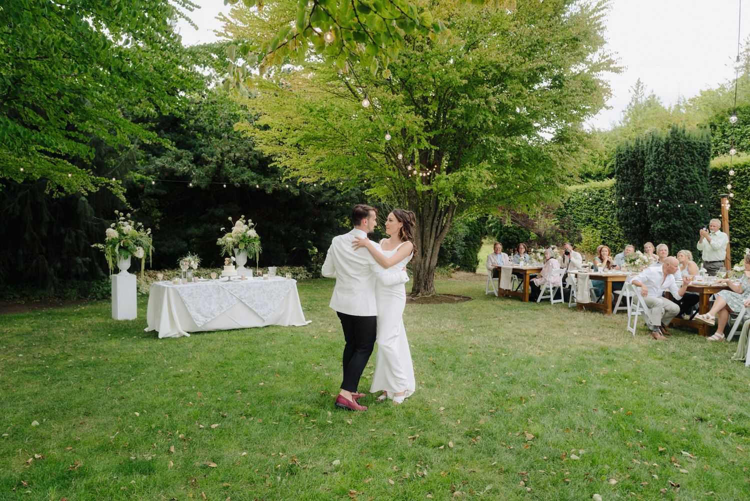 Wedding celebration in a lush green garden setting with guests seated in background.
